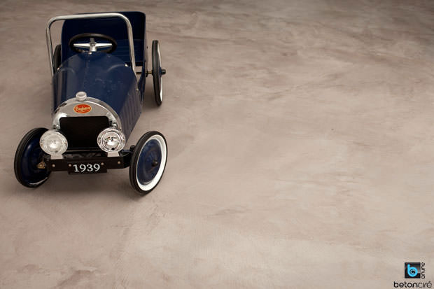 Petite voiture d'enfant en métal posée sur béton ciré gris.