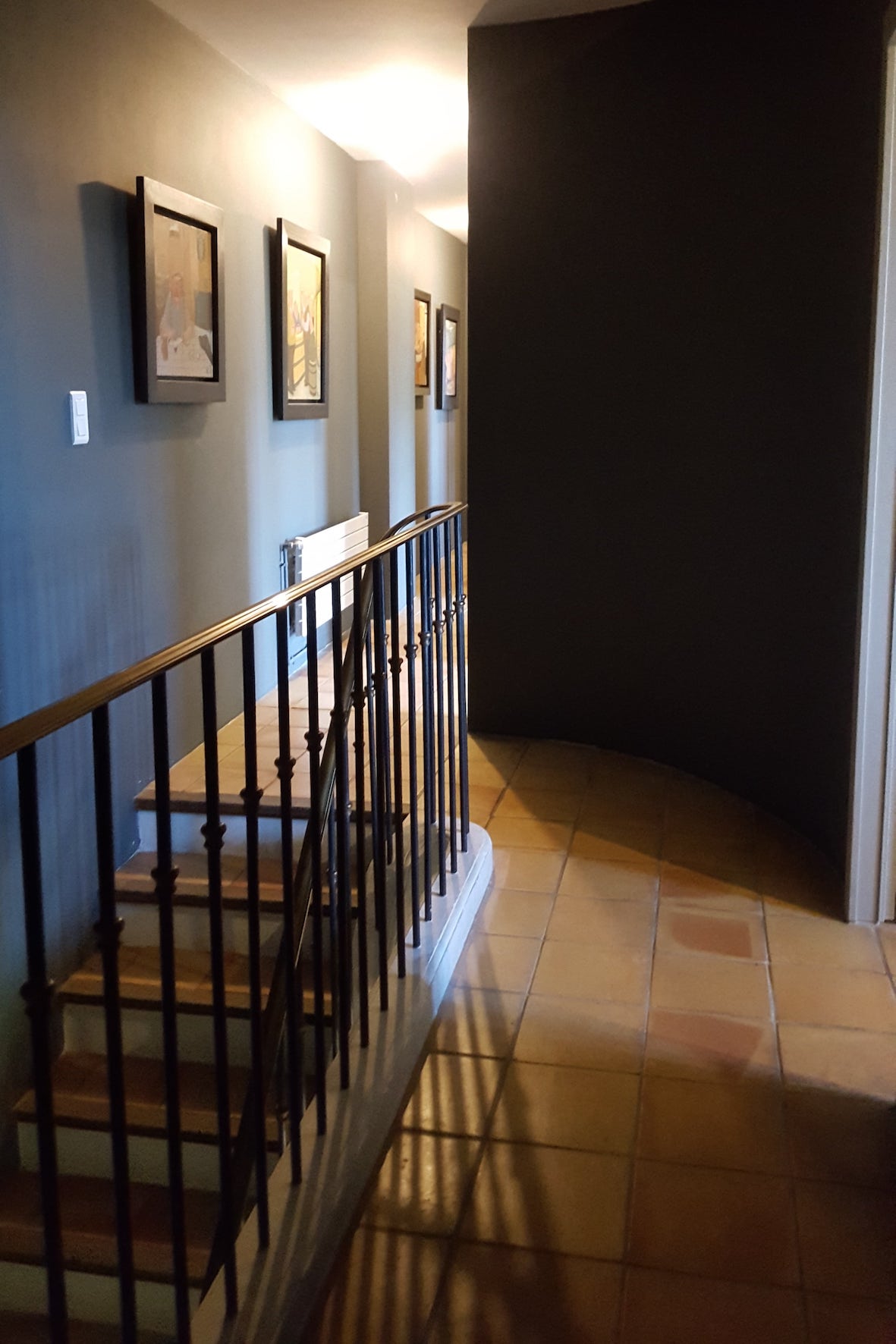 Couloir avec descente d'escalier en terre cuite pale et rampe en fer.